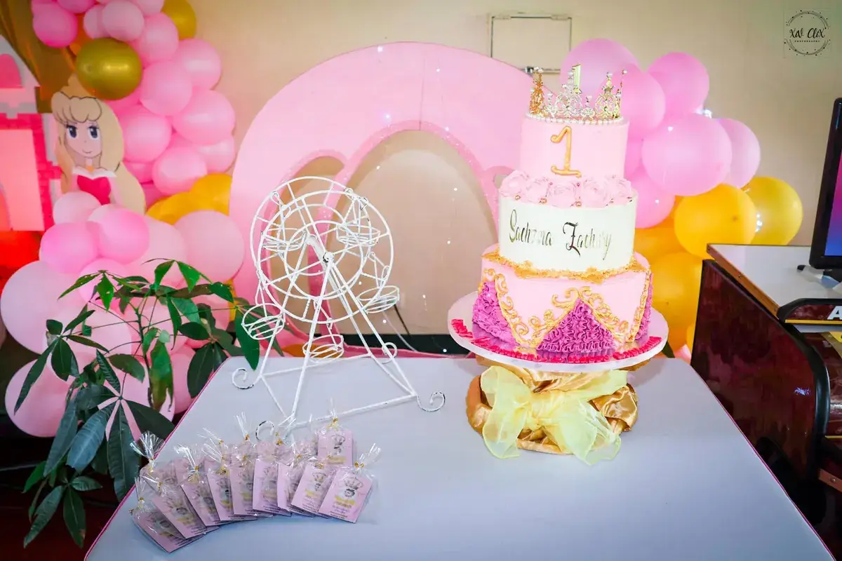 Two-tier pink christening cake with a carousel topper on a styled dessert table