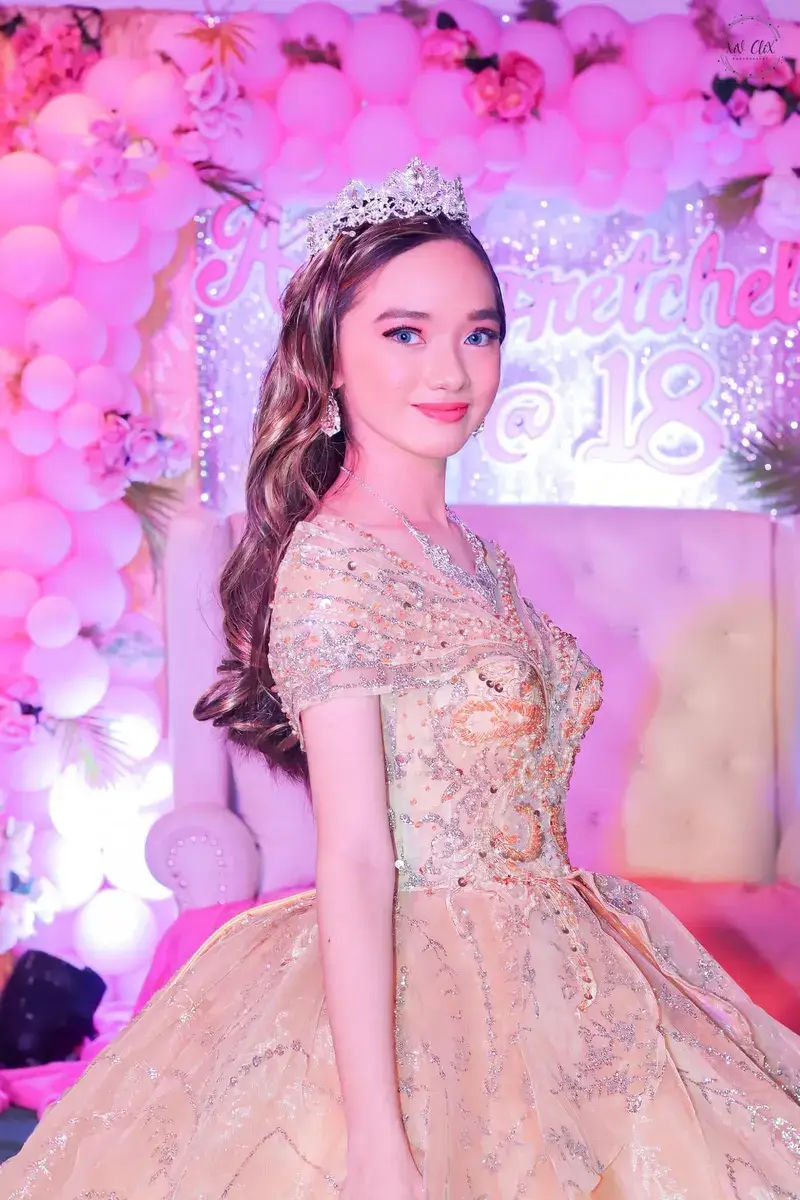 Debutante in a champagne gown in front of a pink balloon and floral backdrop
