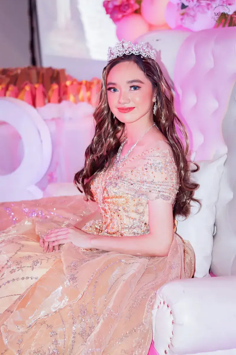 Debutante in a tiara and champagne gown seated on a white throne