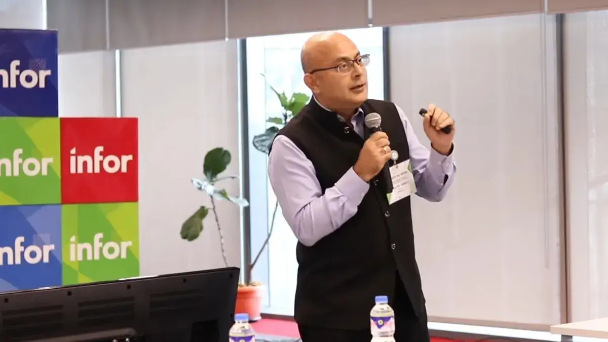 Speaker in a black vest addressing the audience beside colourful event branding