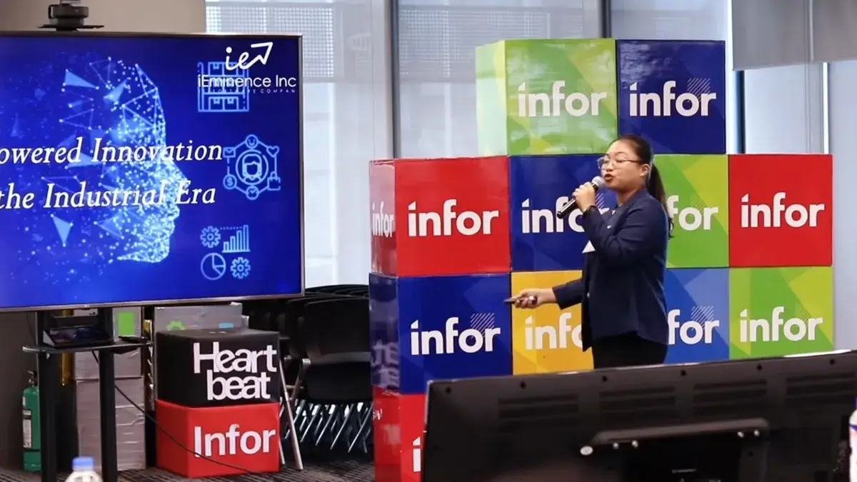 Speaker presenting on stage beside a large screen at a corporate technology conference