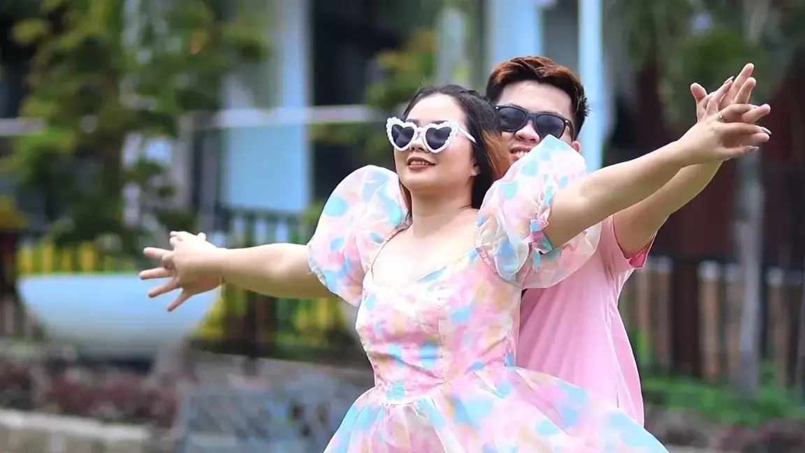 Couple in sunglasses and pastel florals throwing their arms out in a playful pose