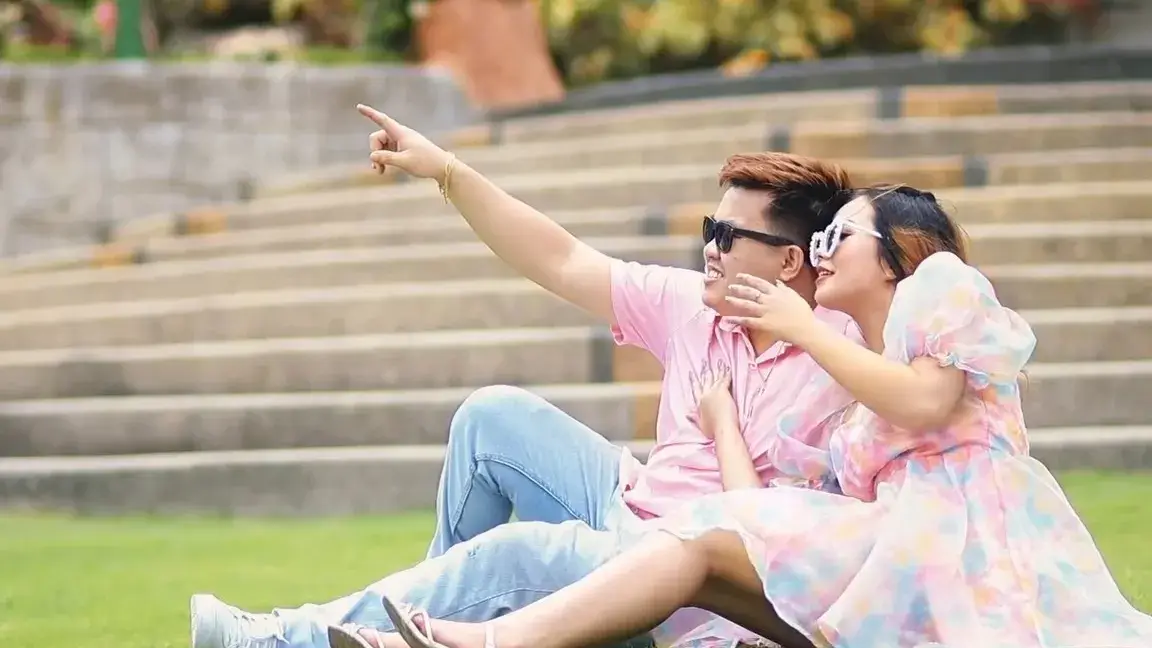 Couple in pastel outfits sitting on garden steps, pointing at the view