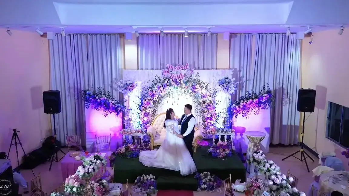 Couple on a flower-filled reception stage lit in lavender and blue