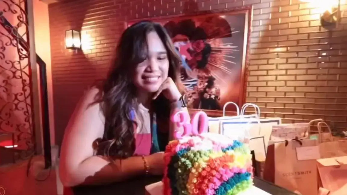 Celebrant smiling beside her 30th birthday cake in a red-lit restaurant