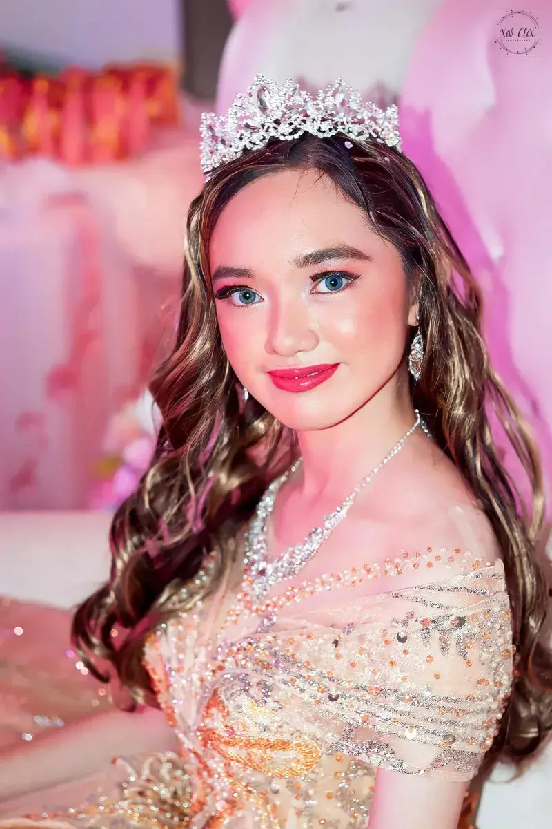Close-up portrait of a debutante with long curled hair and a tiara under warm pink light