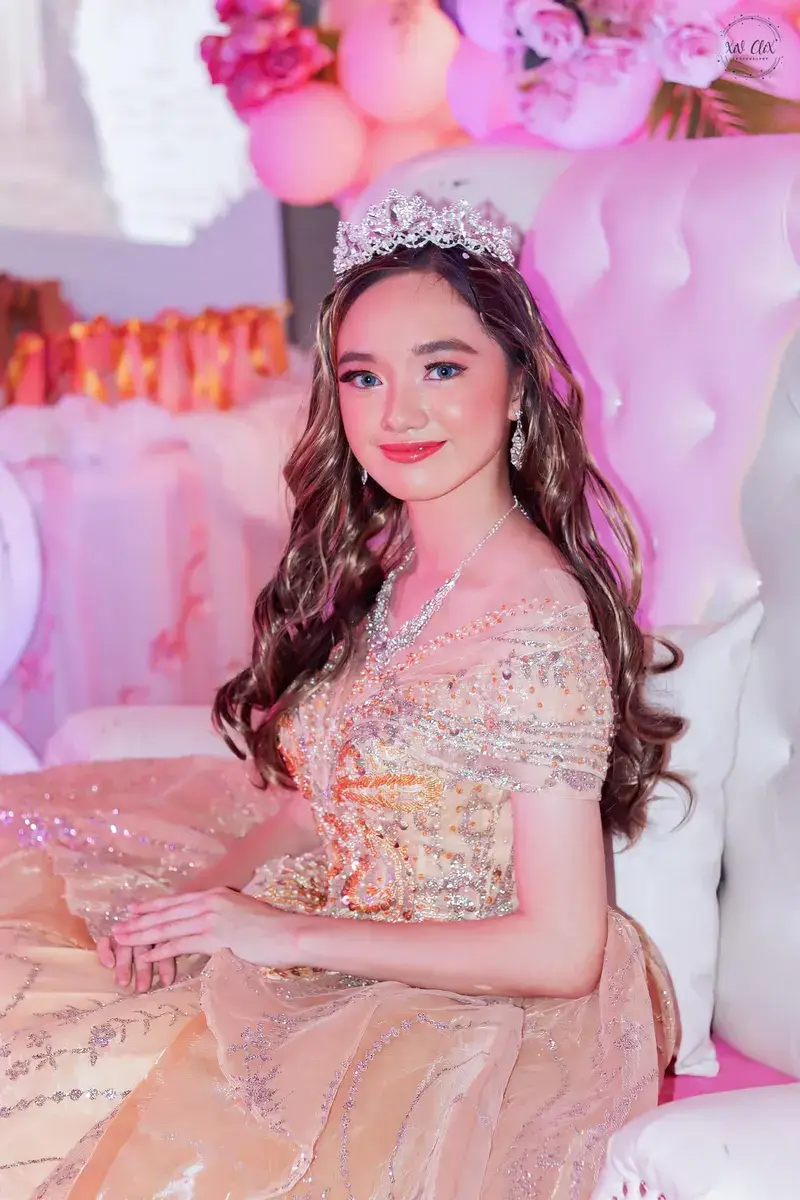 Debutante in a sparkling champagne gown and tiara seated on a white throne